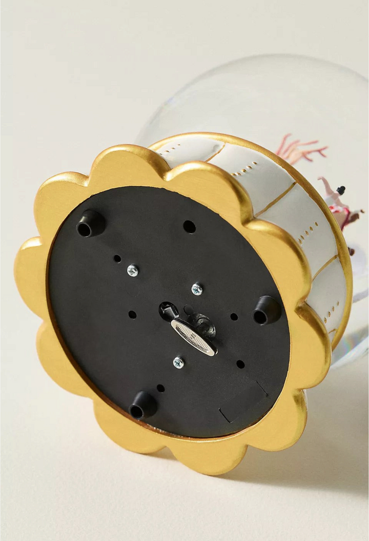 GLAM MODA musical snow globe showing the underside with a gold scalloped base, winding key, and black protective feet.