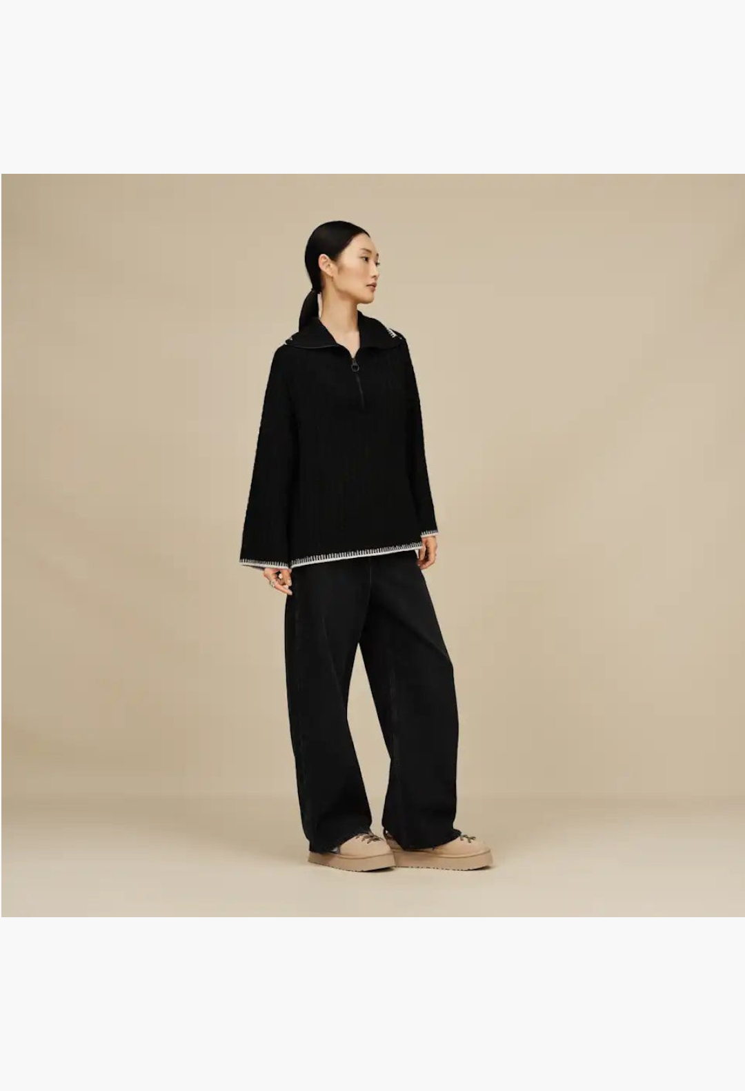 GLAM MODA model wearing a black quarter-zip sweater and wide-leg trousers with tan suede lace-up slippers