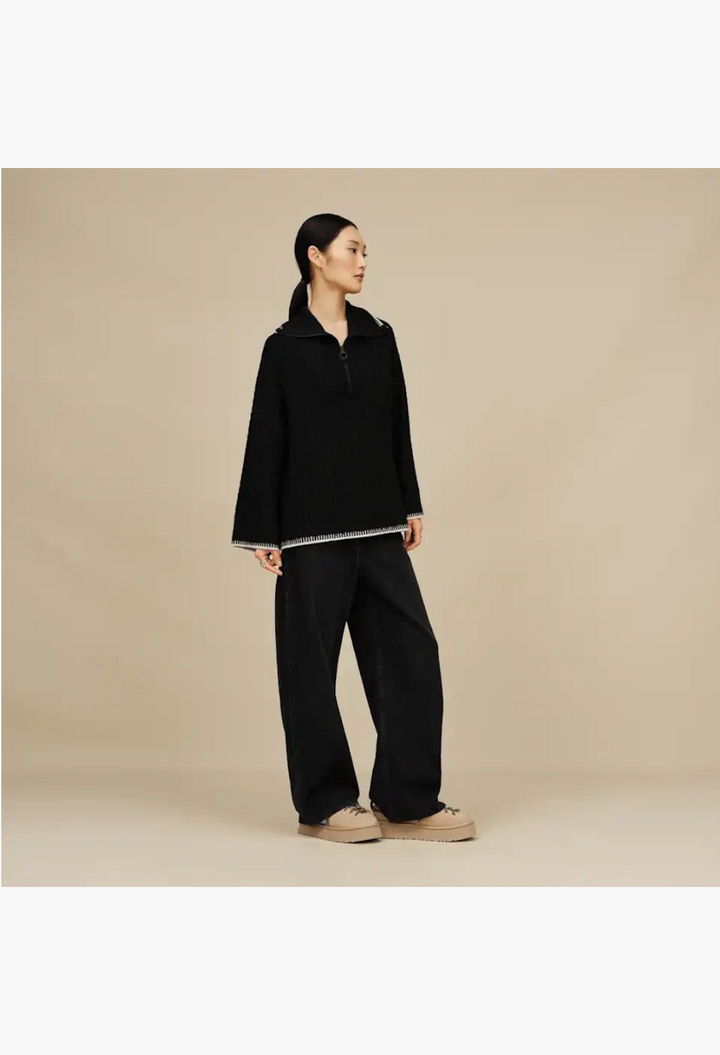 GLAM MODA model wearing a black quarter-zip sweater and wide-leg trousers with tan suede lace-up slippers