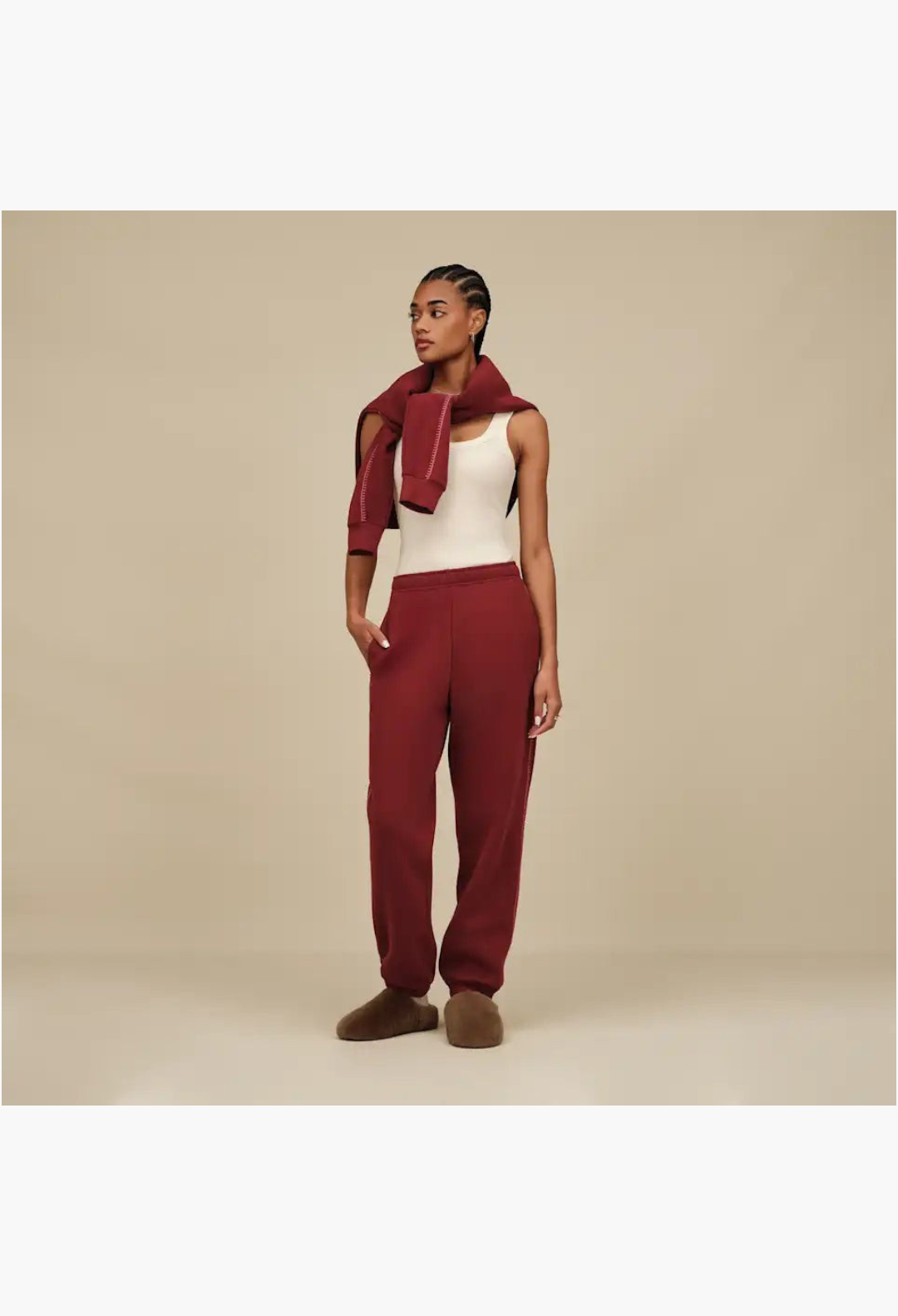 GLAM MODA model wearing maroon sweatpants and cozy brown sheepskin slip-on slippers in a minimalist studio setting