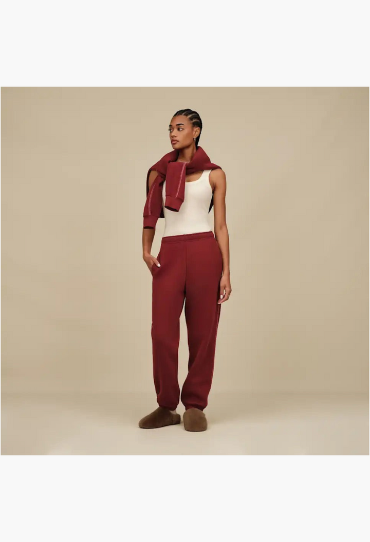 GLAM MODA model wearing maroon sweatpants and cozy brown sheepskin slip-on slippers in a minimalist studio setting