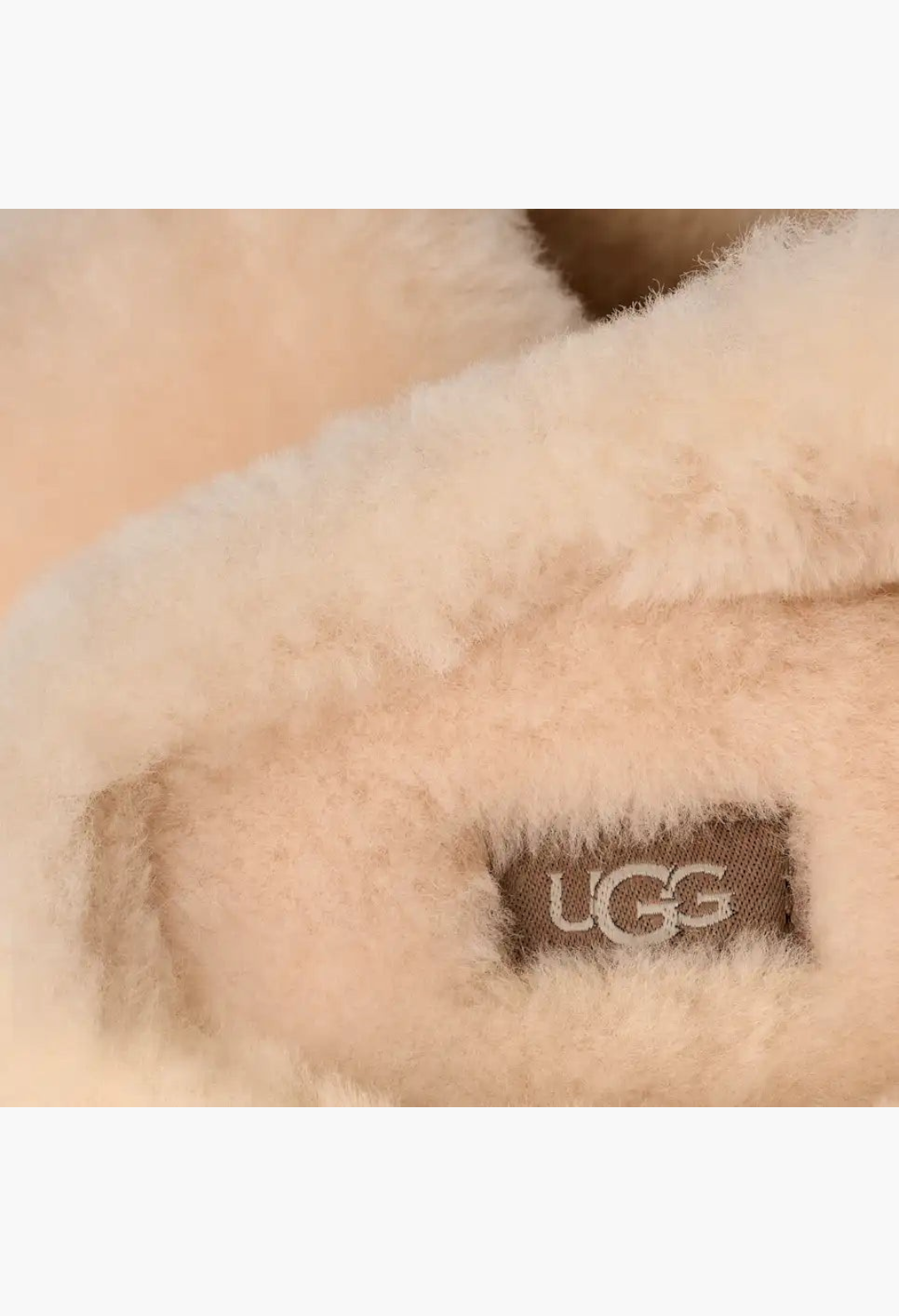 Close-up of GLAM MODA Elea Fluffed Slip-On featuring plush cream sheepskin lining and branded UGG woven insole label.