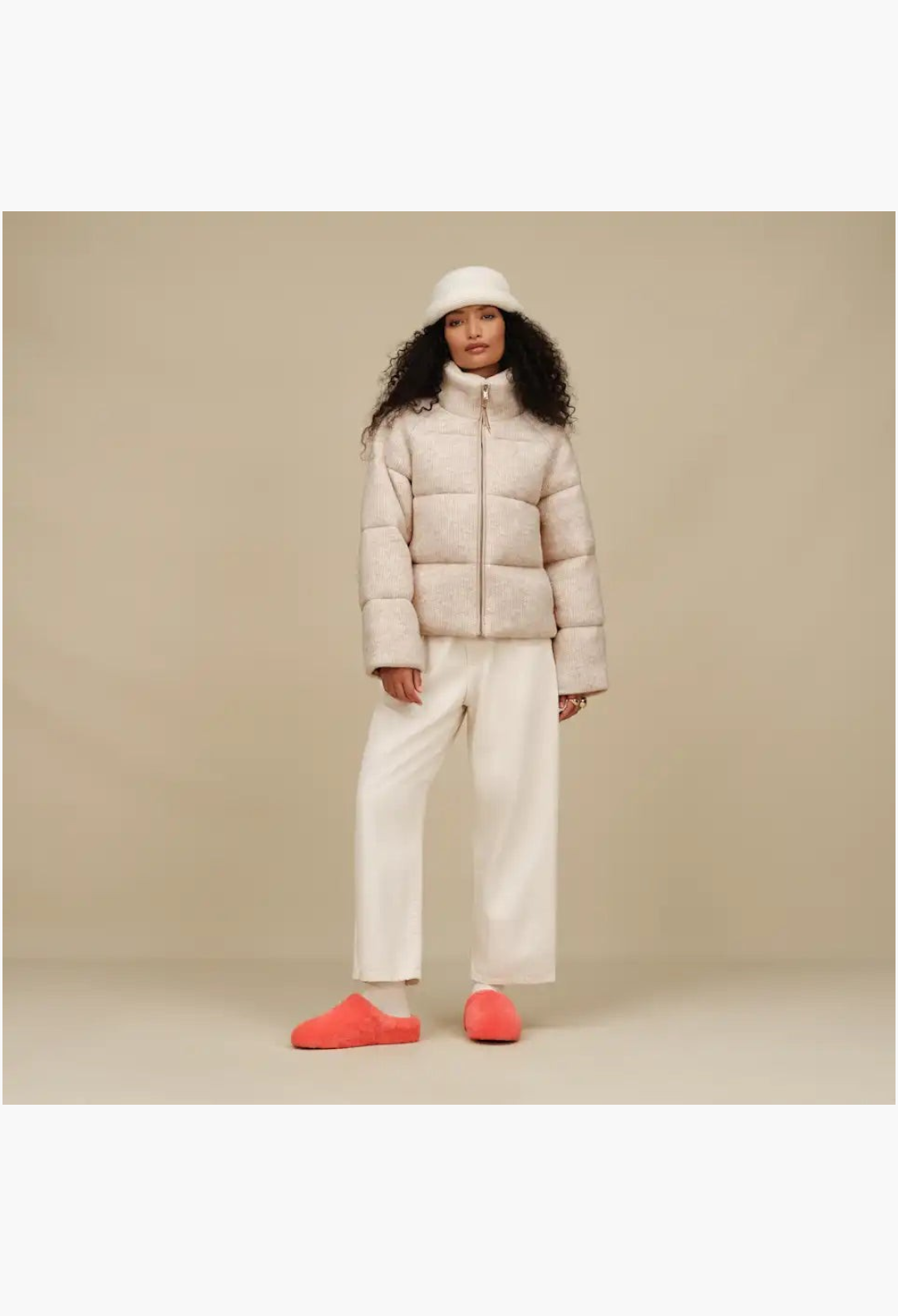 GLAM MODA model wearing a beige puffer jacket and white trousers with bright orange sheepskin Elea slip-on slippers
