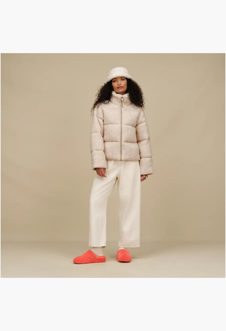 GLAM MODA model wearing a beige puffer jacket and white trousers with bright orange sheepskin Elea slip-on slippers