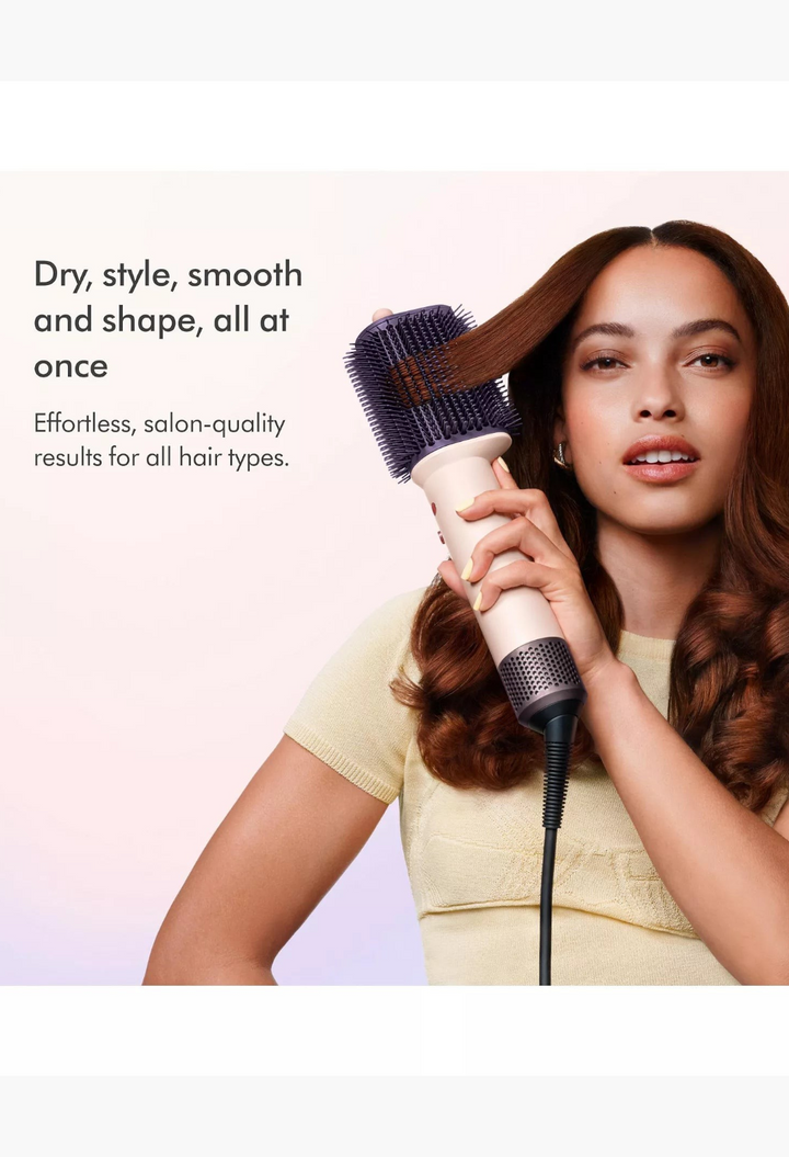 GLAM MODA model using a pink and rose gold Dyson Airsmooth styling brush to smooth a section of her wavy brown hair.