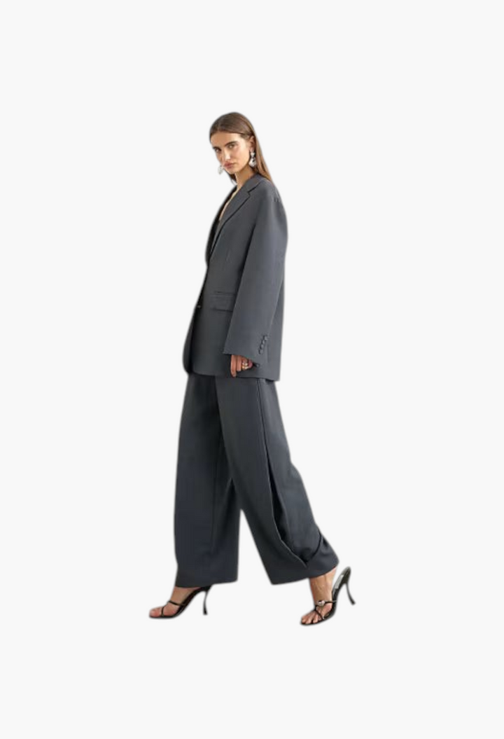 GLAM MODA model wearing grey woven barrel leg trousers with side pleats and a matching oversized blazer