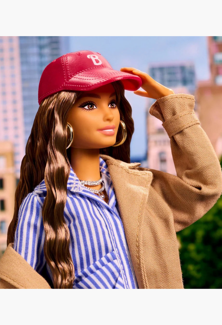 GLAM MODA New York Fashion Week Barbie doll wearing a red cap, beige coat, and blue striped shirt in a city setting.