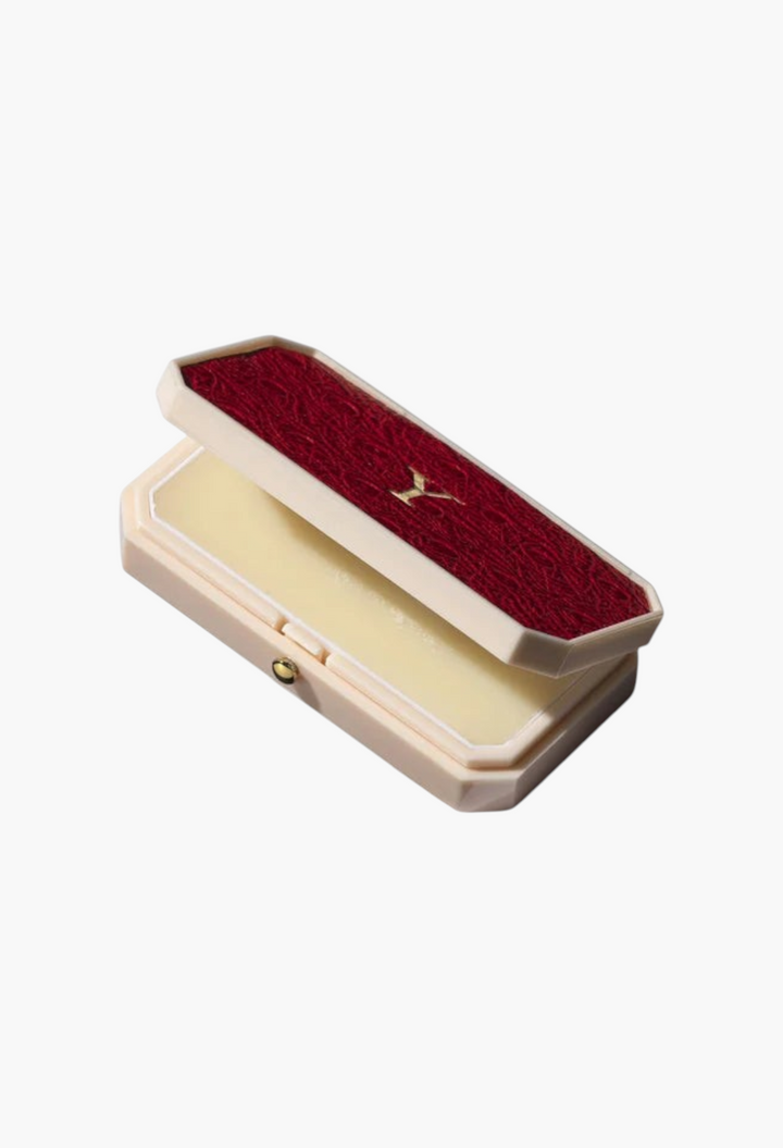GLAM MODA Baume des Muses Ivory lip balm in an elegant cream-colored case with a textured red lid and gold detail.