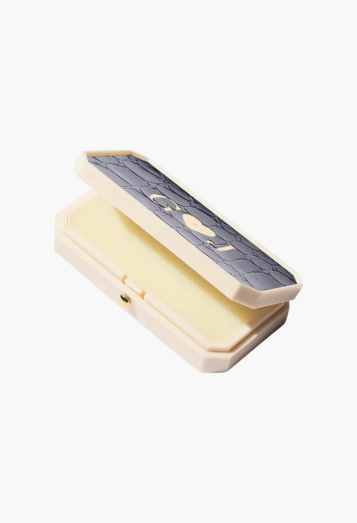 GLAM MODA Baume des Muses Ivory lip balm in a rectangular case with a textured grey lid and gold initial embossing.