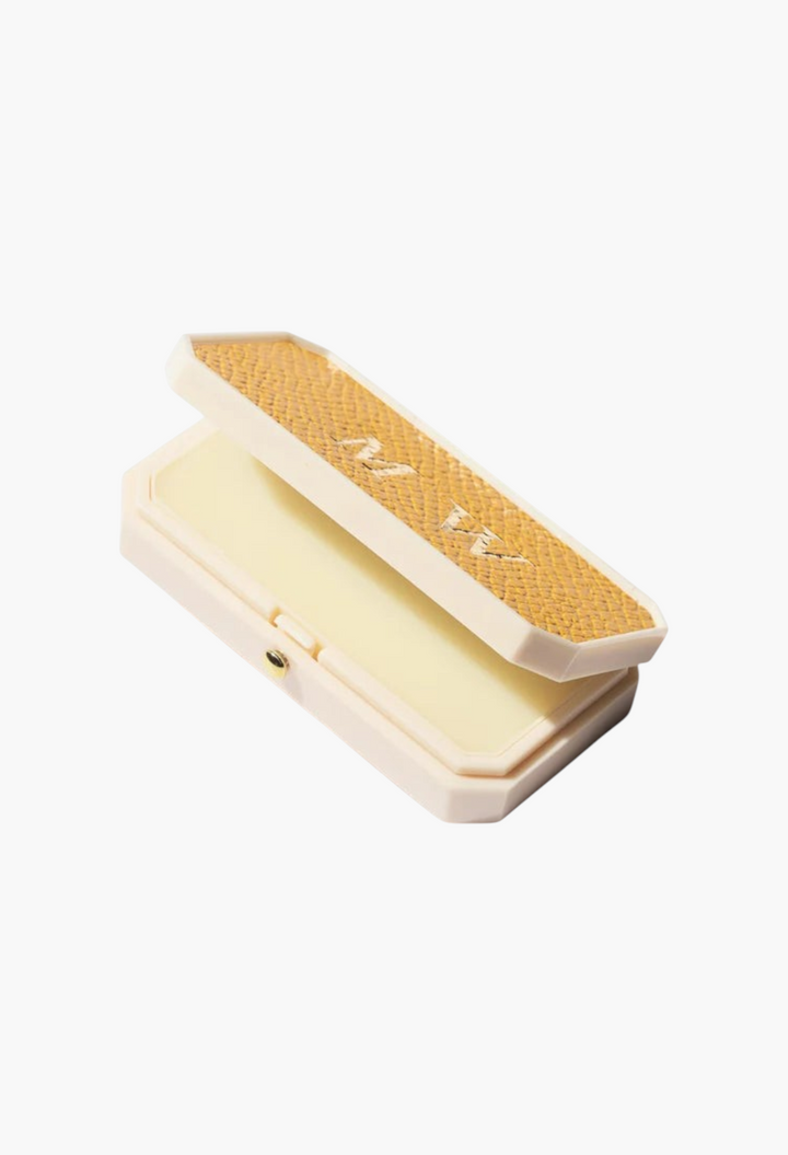 GLAM MODA Baume des Muses Ivory lip balm in a cream-colored case with a textured gold lid and embossed initials.