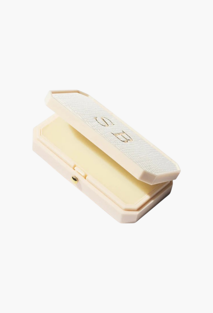 GLAM MODA Baume des Muses Ivory lip balm in an elegant, textured white case with gold embossed initials.