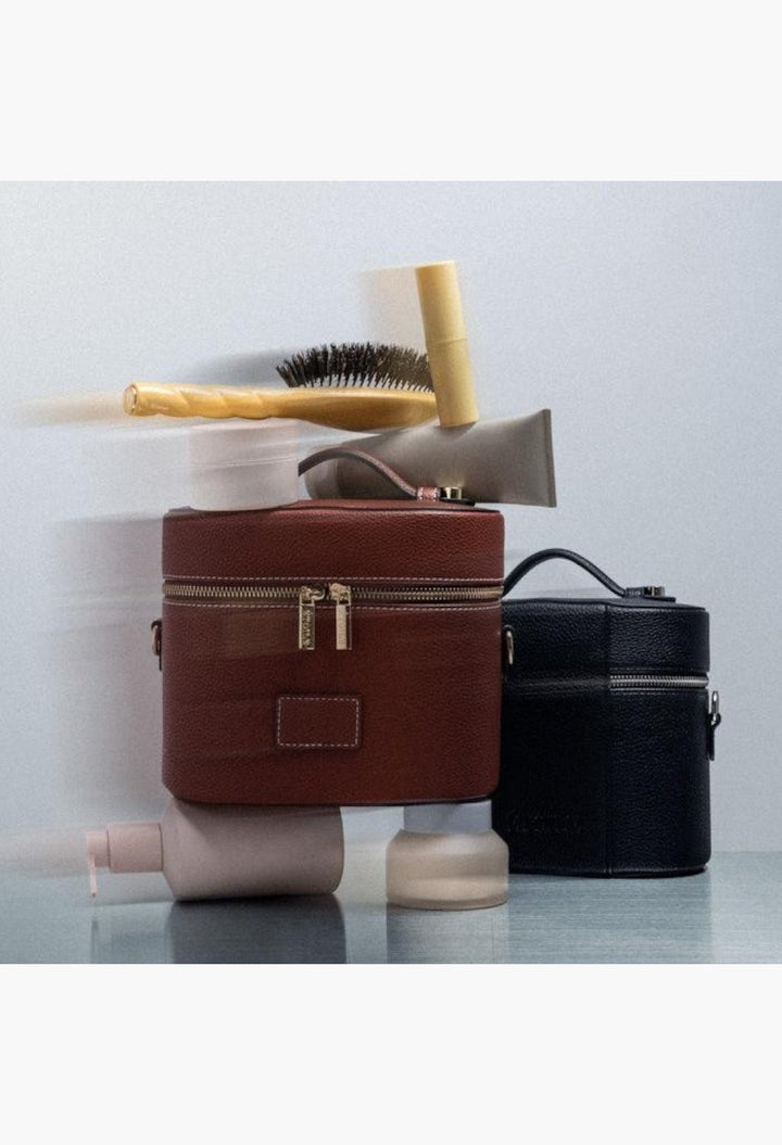 GLAM MODA oval vegan leather toiletry cases in brown and black with beauty products stacked on a reflective surface.