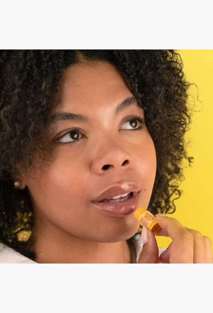 GLAM MODA model applying Burt's Bees tinted lip balm to her lips for a natural, hydrated, and sheer color finish.