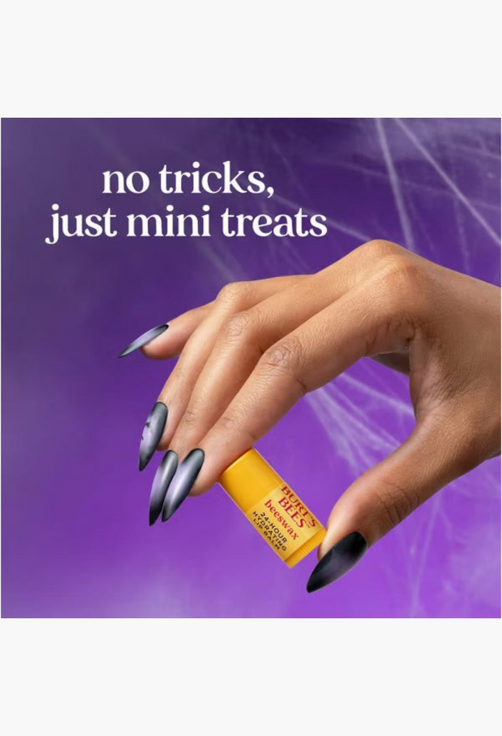 GLAM MODA hand holding a yellow Burt's Bees tinted lip balm tube with long dark stiletto nails