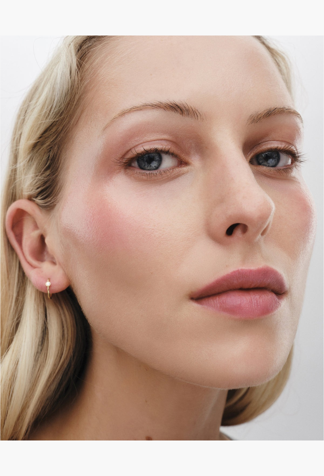 GLAM MODA Lit Up Highlight Stick applied to a model's cheekbones for a radiant, glassy, and hydrated finish.