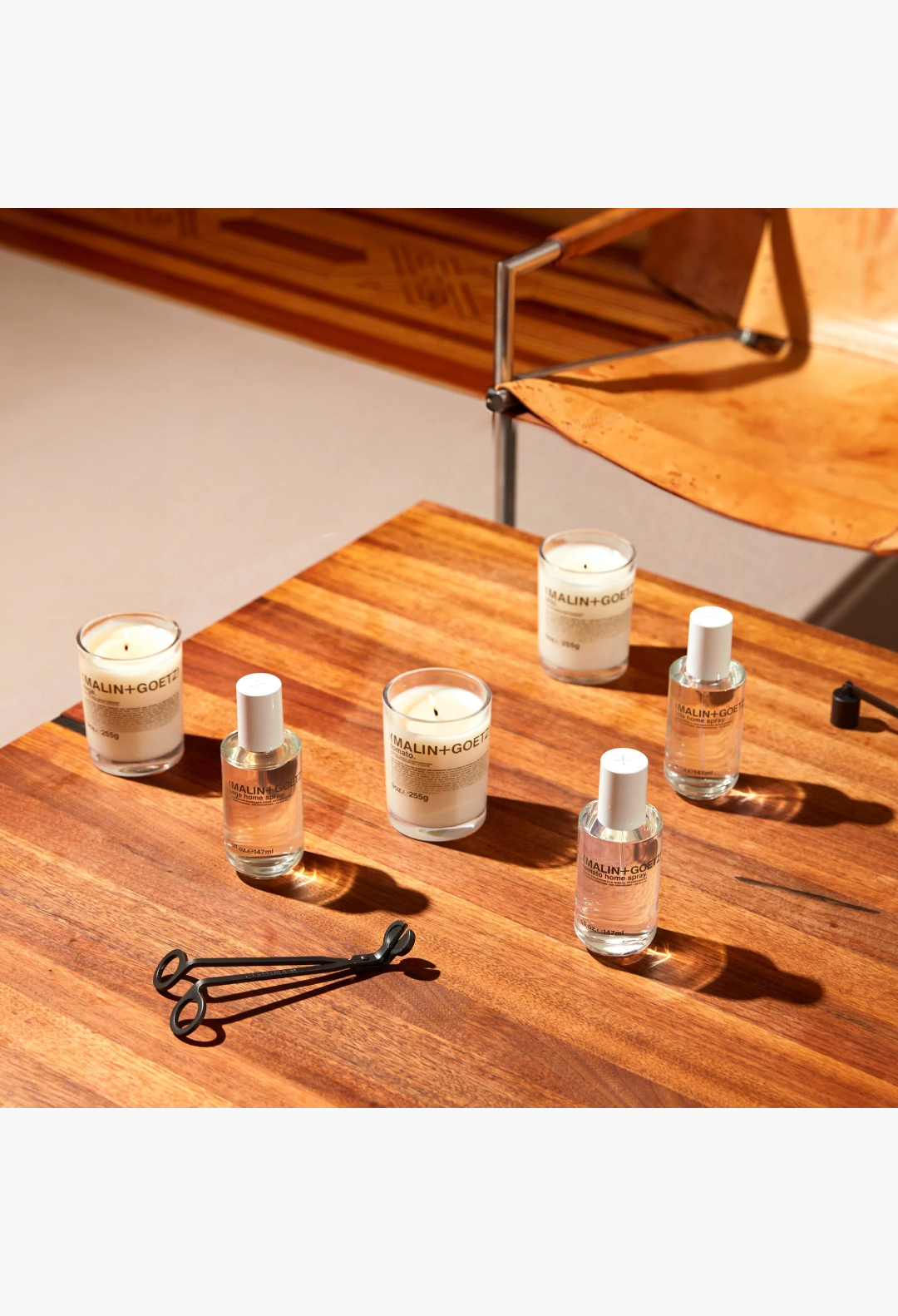 GLAM MODA collection of Malin + Goetz Otto home sprays and candles with a black metal wick trimmer on a white background