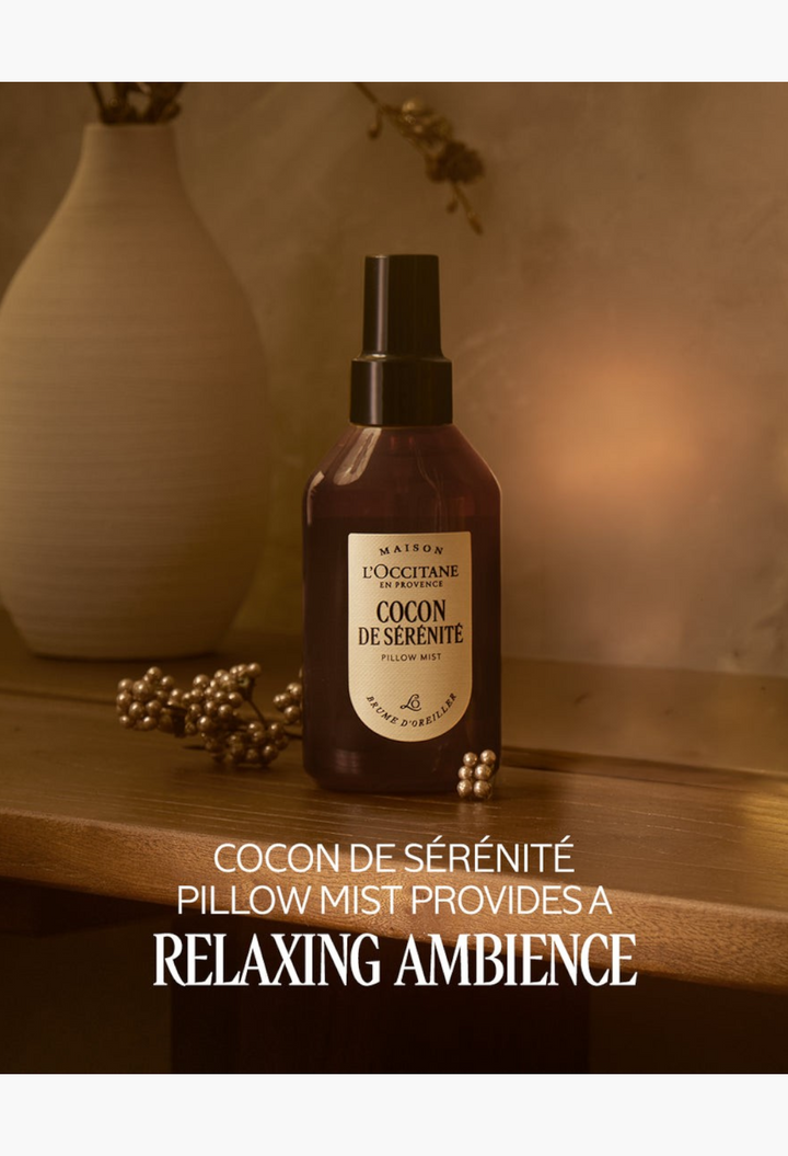 GLAM MODA L'Occitane Cocon de Sérénité pillow mist in a brown bottle on a wooden table with a vase and gold decor