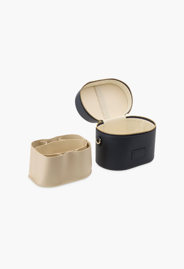GLAM MODA oval toiletry case in black vegan leather with a removable beige divider insert and gold zipper detail.