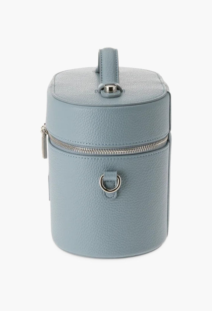 GLAM MODA oval toiletry case in light blue vegan leather with a top handle, silver hardware, and shoulder strap rings.