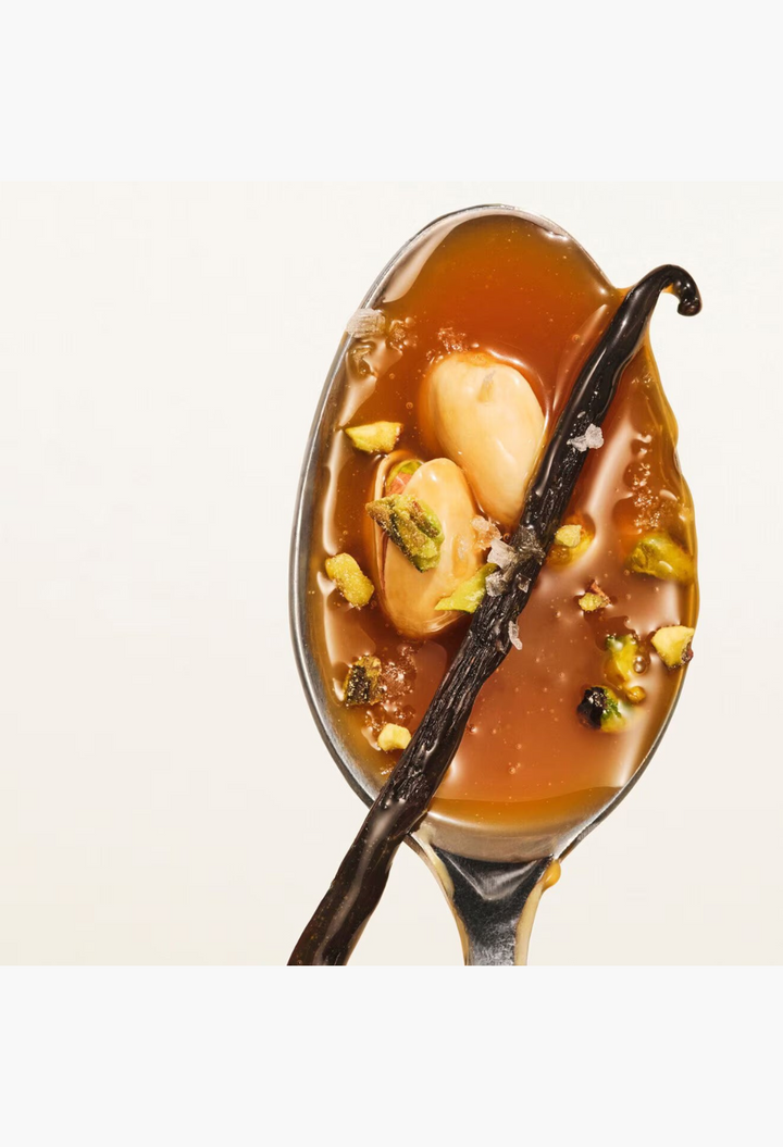 GLAM MODA Body & Sol ingredients featuring a silver spoon filled with caramel sauce, vanilla bean, and crushed pistachios