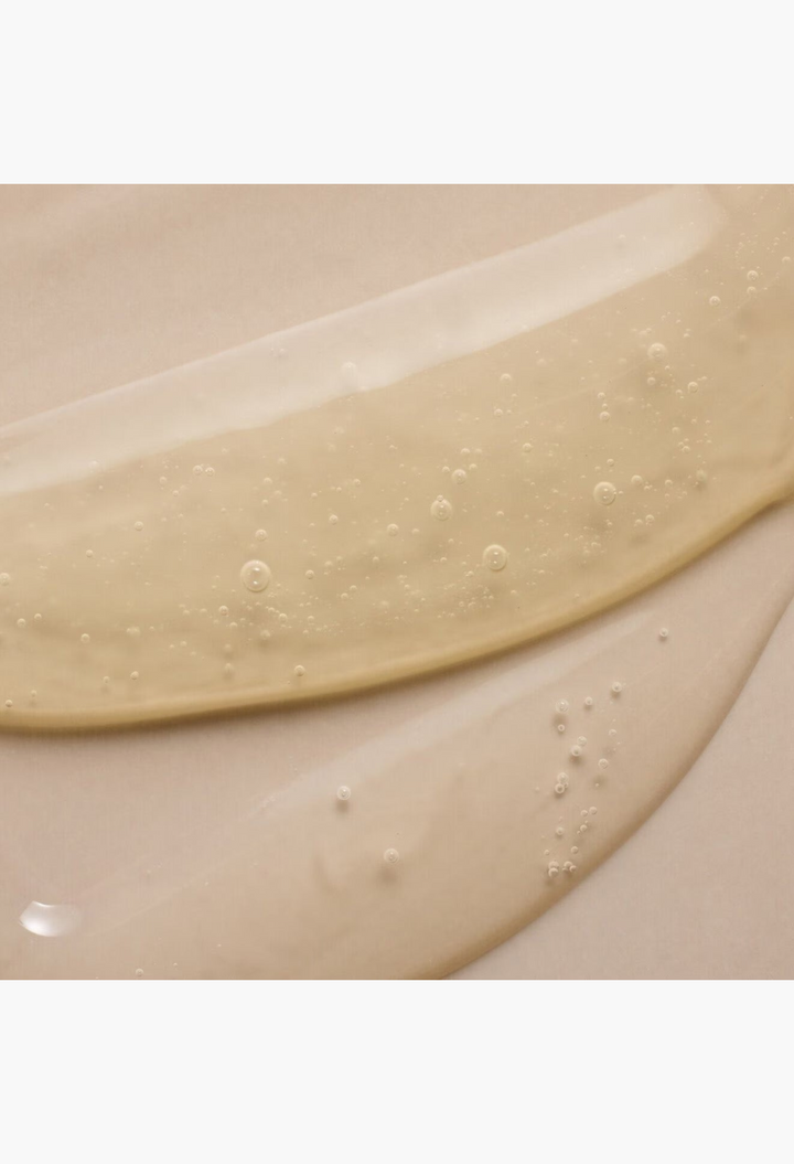 GLAM MODA GRO revitalizing shampoo texture showing a clear, golden-hued gel formula with small air bubbles.