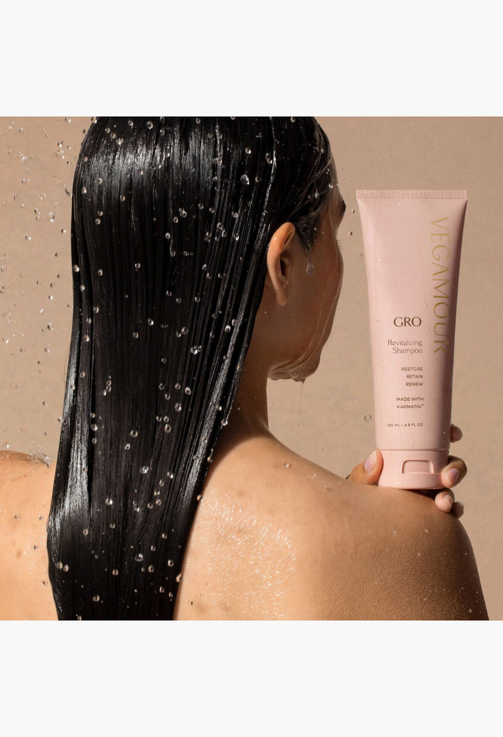 GLAM MODA GRO Revitalizing Shampoo tube held by a woman with wet, long hair in a shower setting.