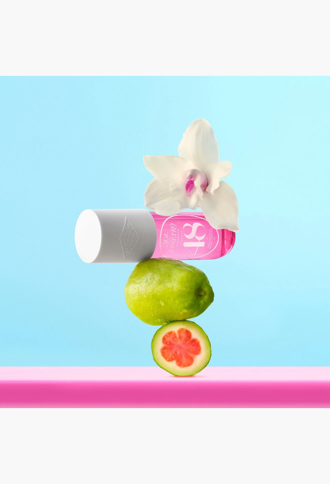 GLAM MODA Cheirosa 48 perfume mist bottle balanced with a fresh guava fruit and a white orchid on a blue background