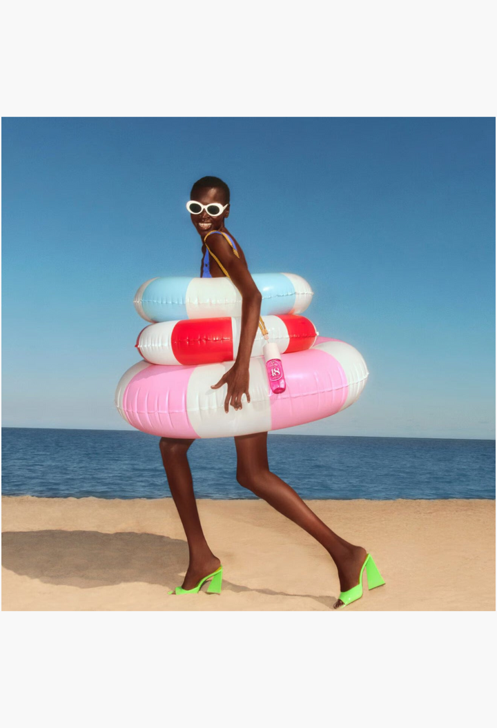 GLAM MODA model wearing white sunglasses and lime heels, holding a Cheirosa 48 Perfume Mist with pool floats.