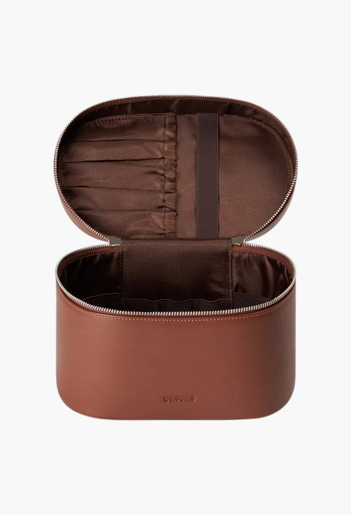 GLAM MODA oval espresso brown vegan leather vanity case with silver zipper and interior brush storage compartments.