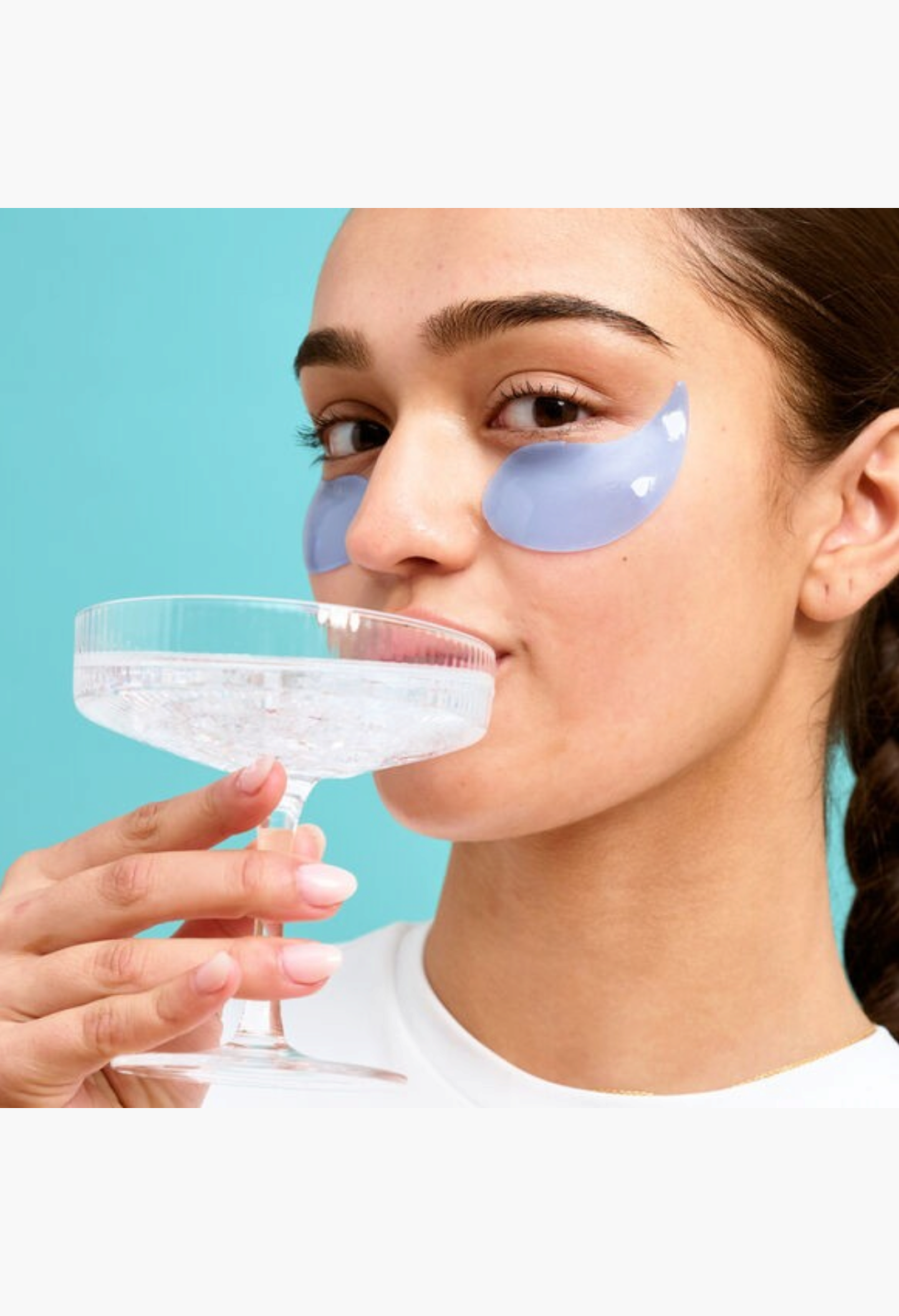 GLAM MODA Patchology Serve Chilled eye gels on a woman holding a cocktail glass against a blue background