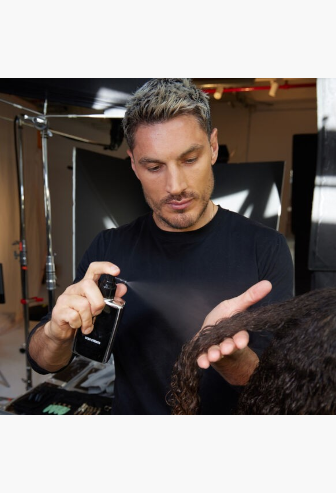 GLAM MODA stylist applying Color Wow Extra Strength Dream Coat anti-humidity spray to curly hair for a sleek finish.