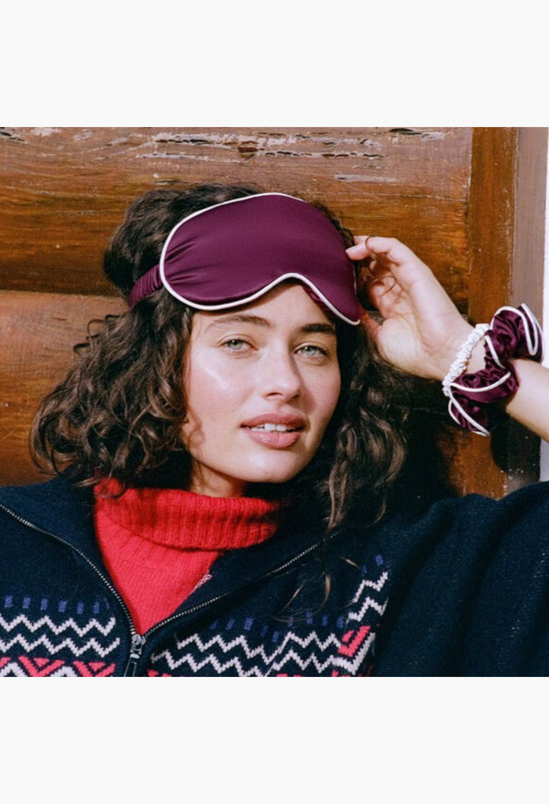GLAM MODA silk sleep mask and scrunchie set in crimson, worn by a woman with curly hair for lash and hair protection.