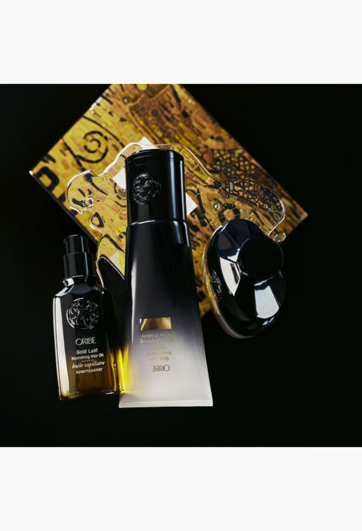 GLAM MODA Oribe Gold Lust haircare set featuring shampoo, conditioner, and nourishing hair oil on a black background.