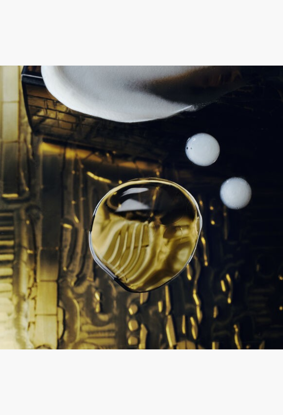 GLAM MODA Oribe Gold Lust nourishing hair oil with a rich golden texture and white droplets on a dark reflective surface