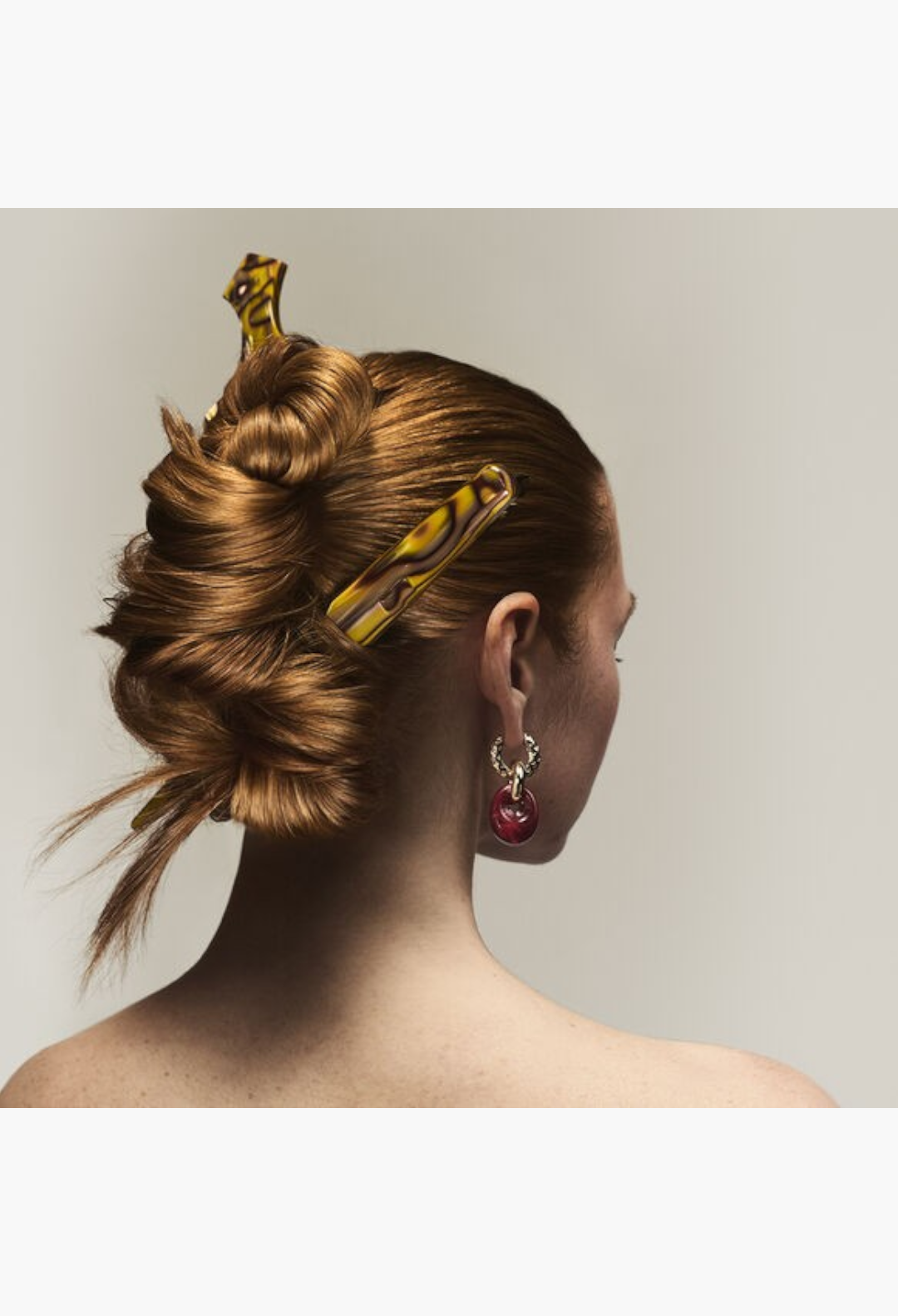 GLAM MODA model with auburn hair styled in an intricate updo secured with tortoiseshell hair clips and red earrings