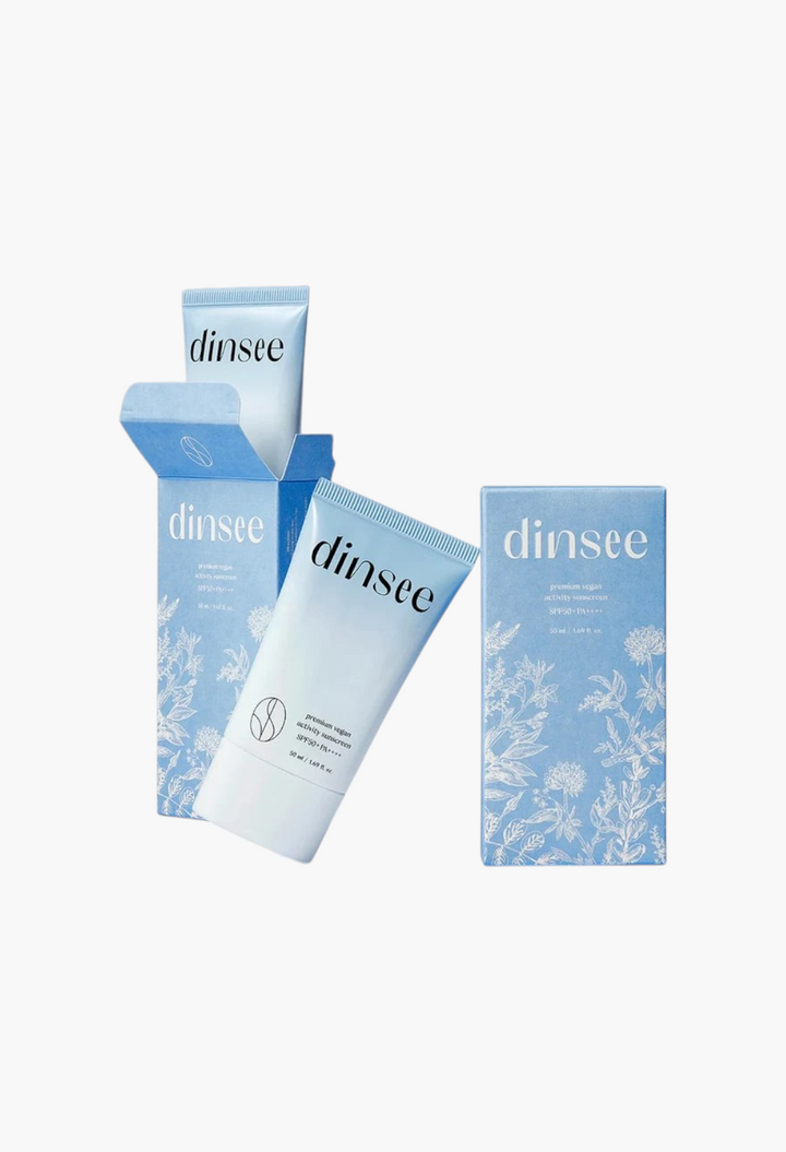 GLAM MODA Dinsee vegan SPF50+ activity sunscreen tubes and floral-patterned blue packaging on a light blue background.