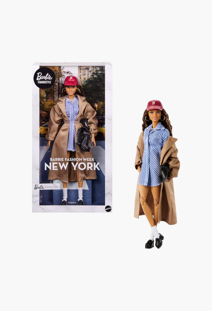 GLAM MODA New York Fashion Week Barbie doll wearing a tan trench coat, striped shirt dress, and red baseball cap.