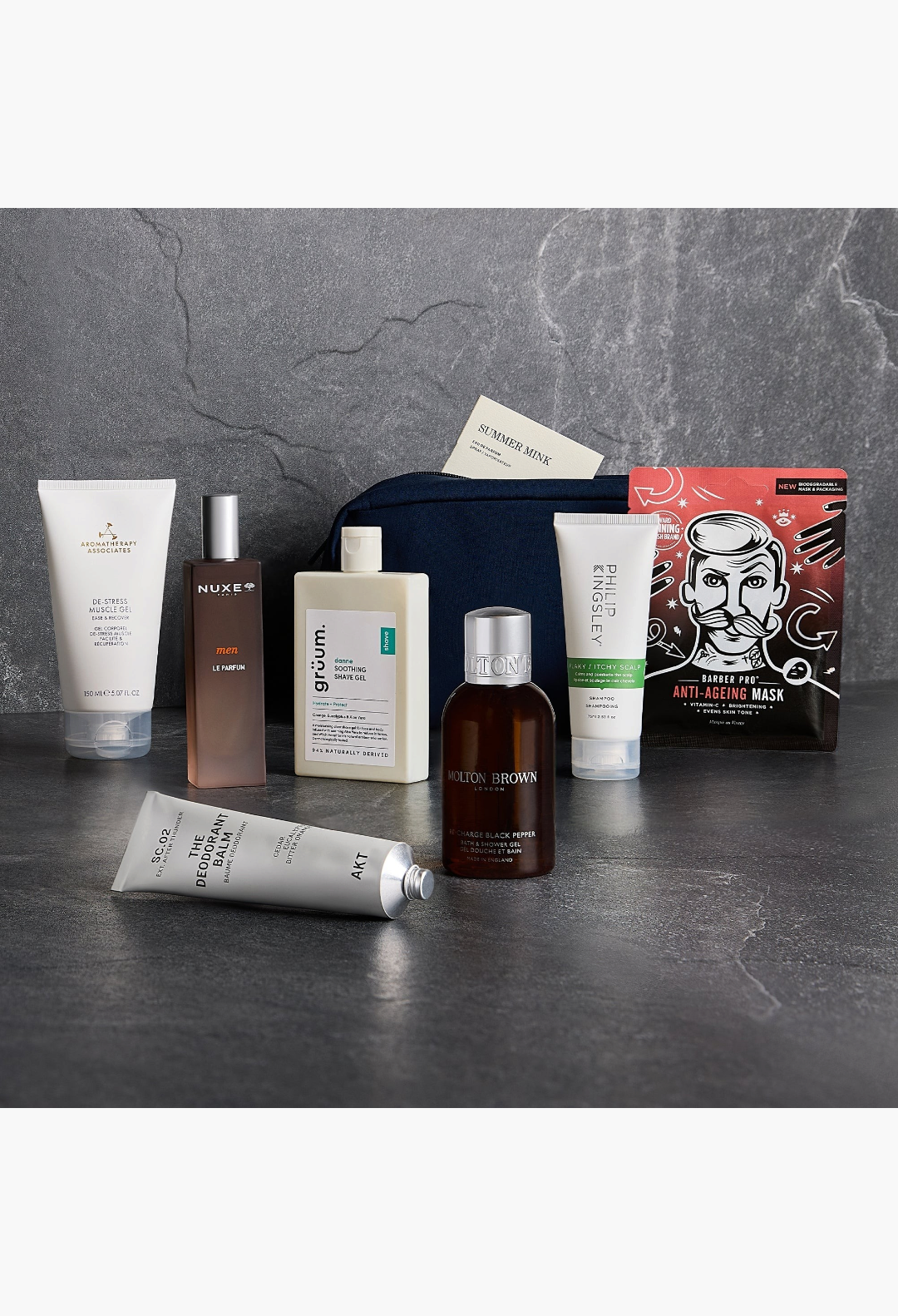 GLAM MODA GLOSSYBOX Grooming Kit featuring skincare and haircare products in a navy bag on a dark stone surface.