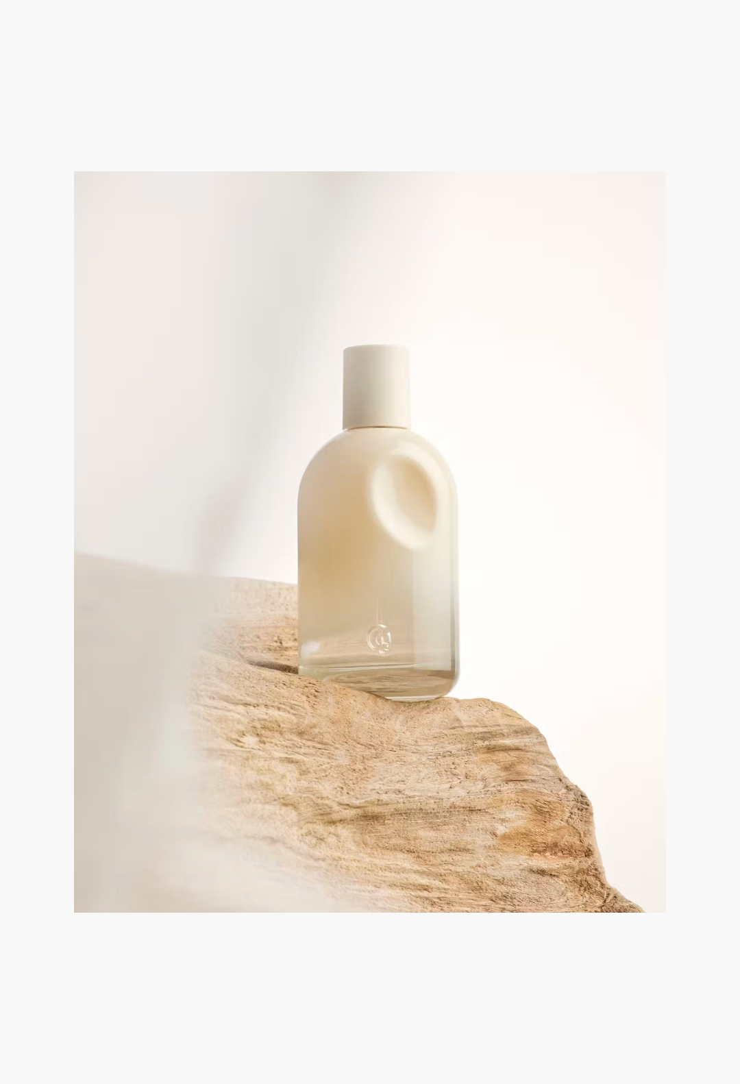 GLAM MODA Glossier You Doux woody eau de parfum in a minimalist glass bottle resting on a textured piece of driftwood.