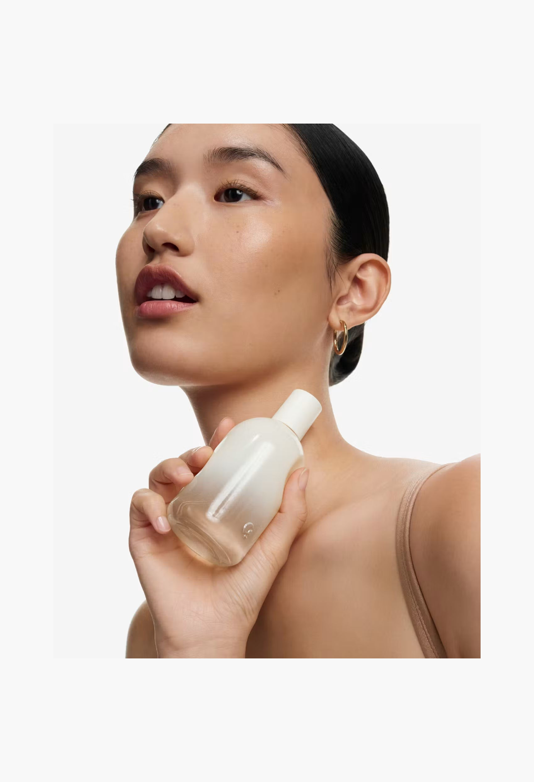 GLAM MODA model holding a bottle of Glossier You Doux woody eau de parfum against her neck