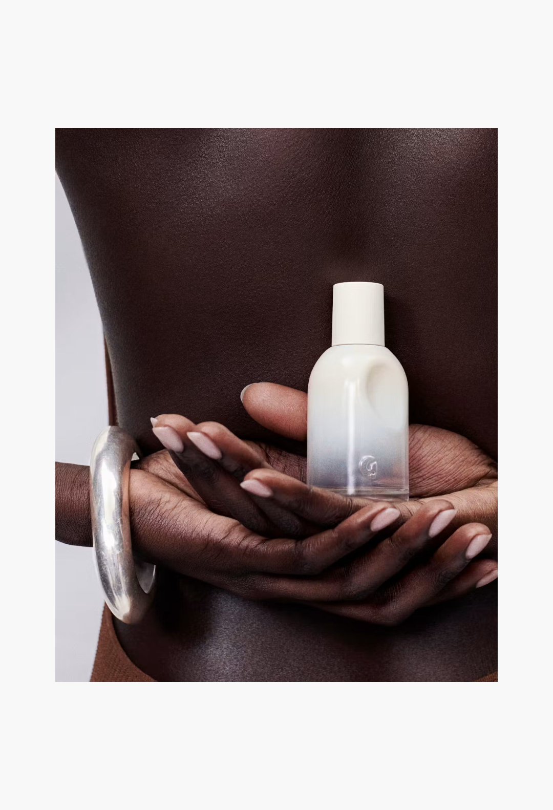 GLAM MODA Glossier You Doux woody eau de parfum bottle held in hands against a person's back with a silver bracelet.