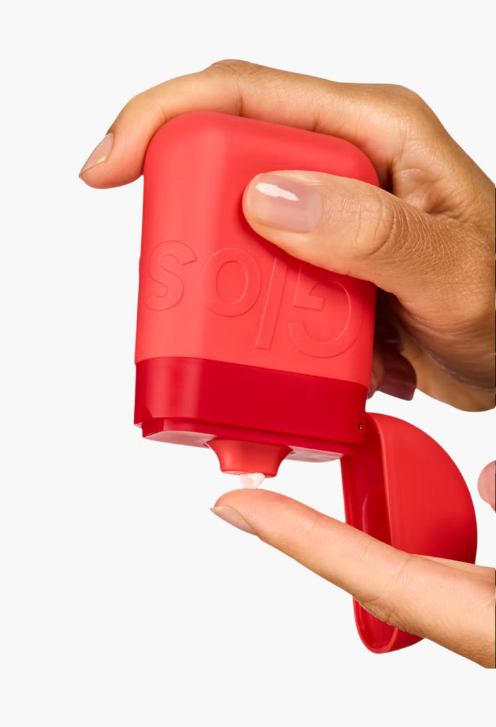 GLAM MODA red palm-sized hand cream pod with a squeeze-to-dispense cap being used on a finger