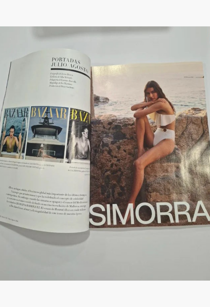 GLAM MODA Bazaar Spain July 2026 magazine spread featuring a model in a white bikini on a rocky Mediterranean beach