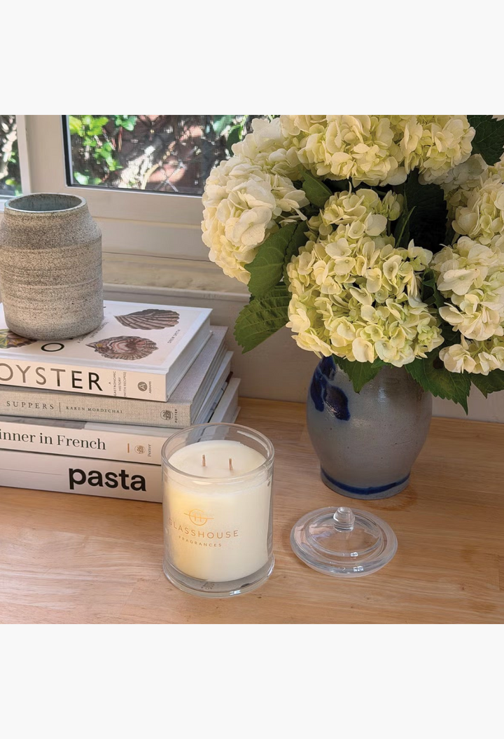 GLAM MODA Glasshouse Fragrances Flower Therapy soy wax candle in a glass jar next to a vase of white hydrangeas
