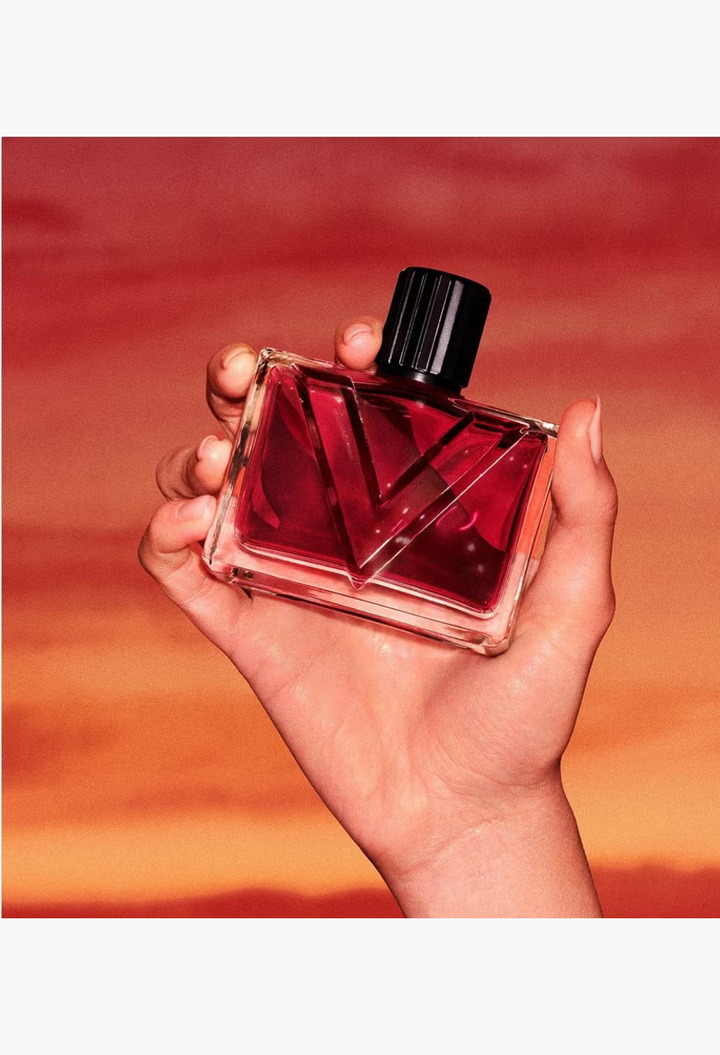 GLAM MODA Valentino Vendetta Donna perfume bottle held in hand against a vibrant sunset background