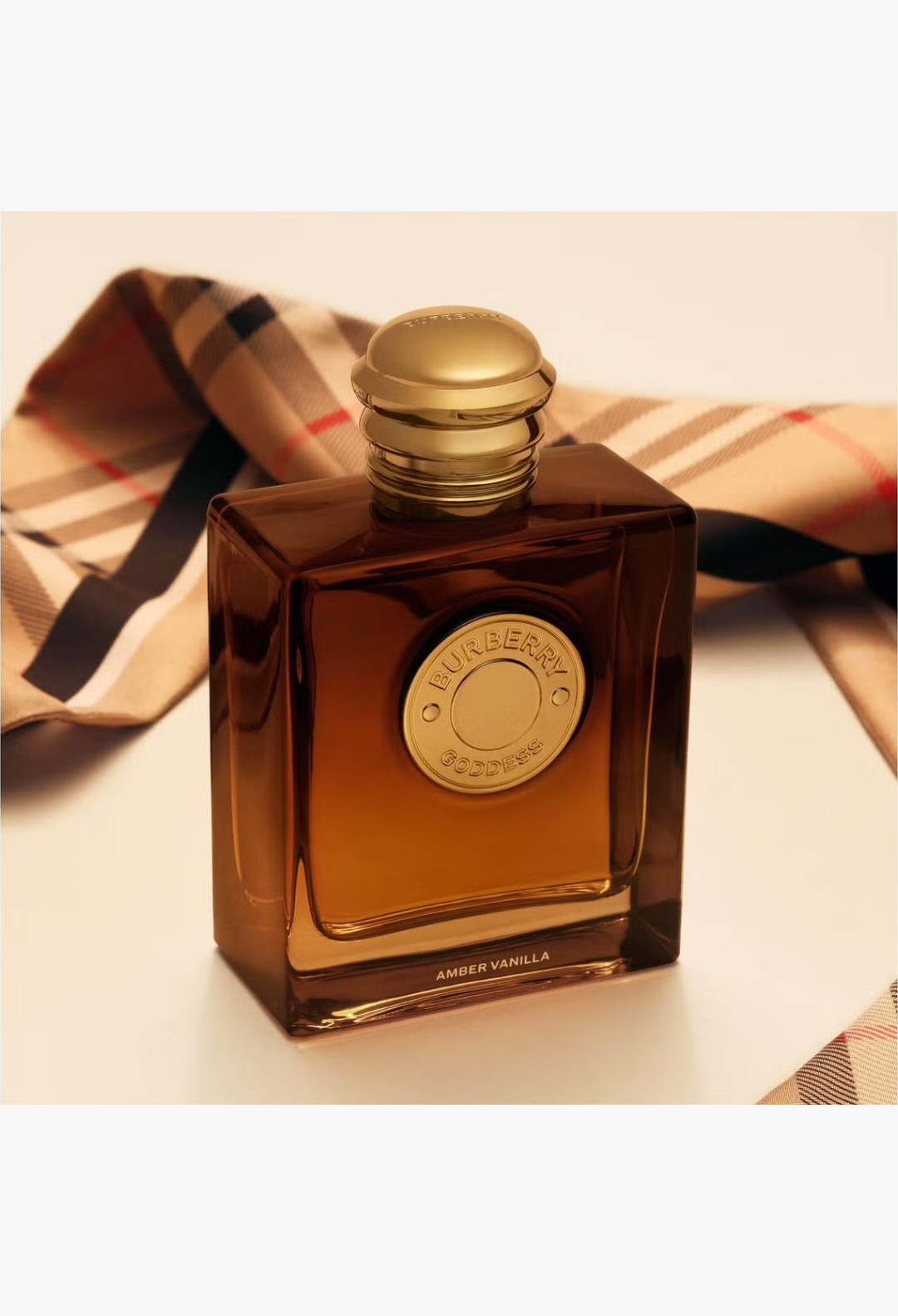 GLAM MODA Burberry Goddess Amber Vanilla perfume bottle with golden cap and medallion on a signature check fabric