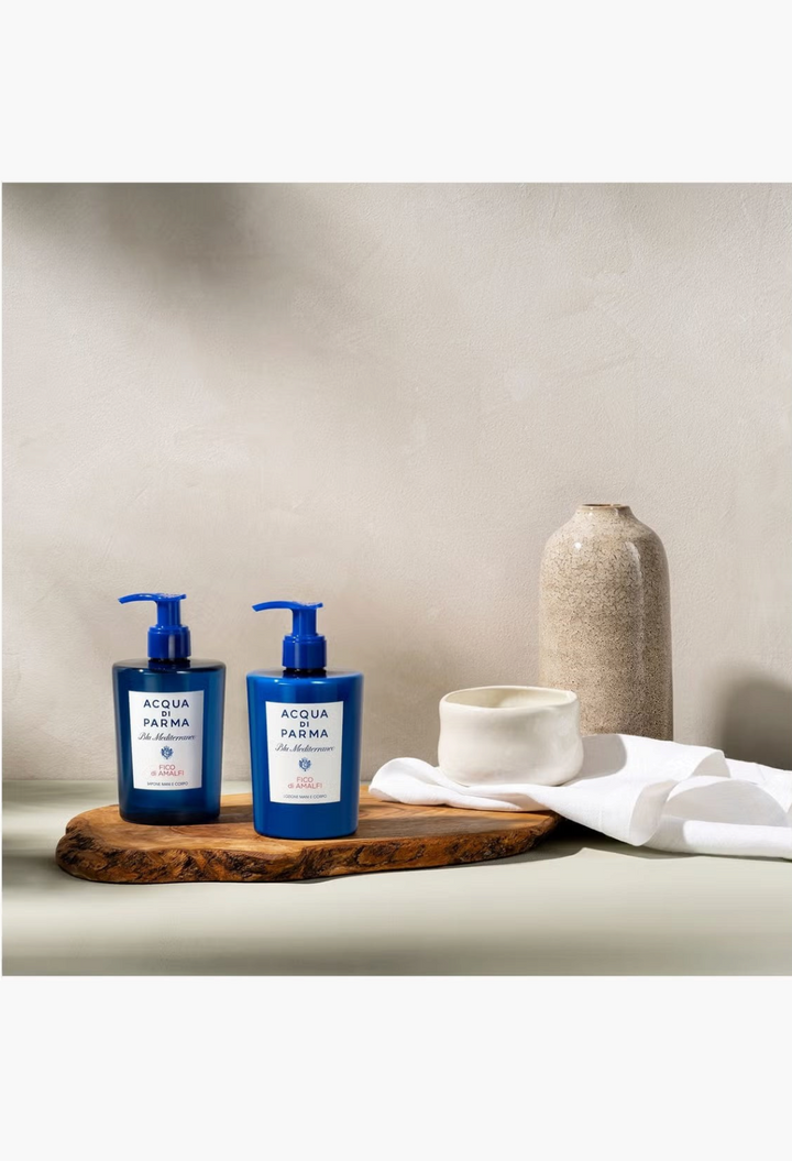 GLAM MODA Acqua Di Parma Fico di Amalfi hand and body wash bottles on a wooden board with decorative ceramic vases.
