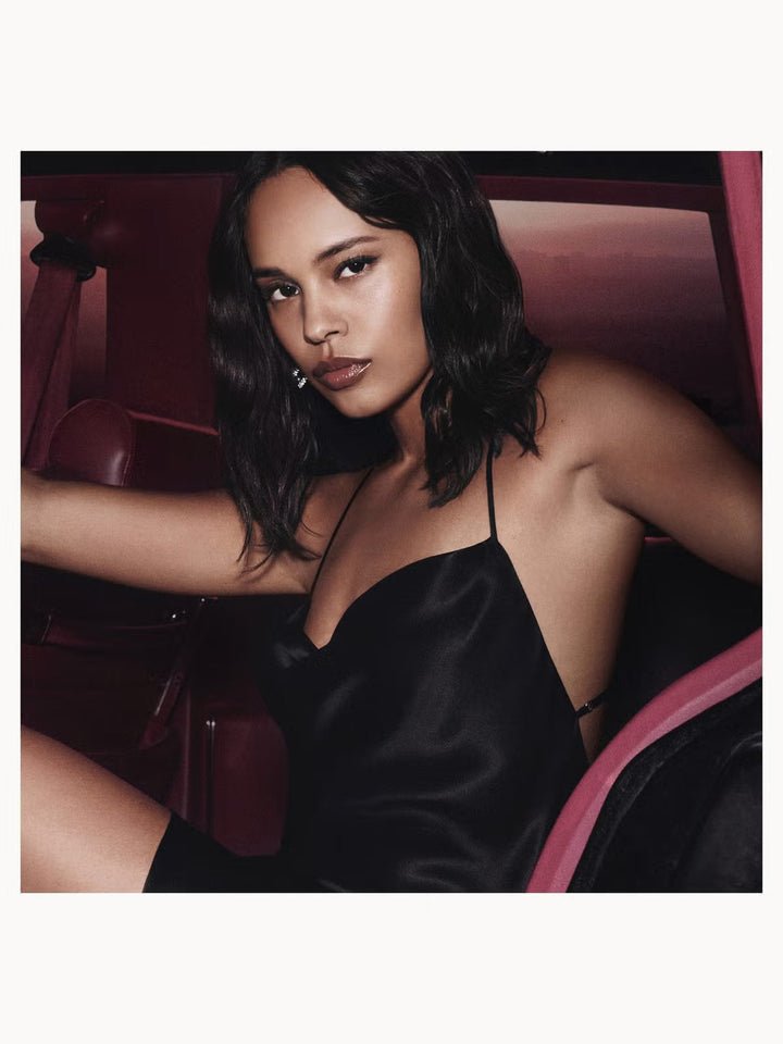 GLAM MODA model wearing a black satin slip dress posing next to the YSL Black Opium Pink Glaze perfume bottle
