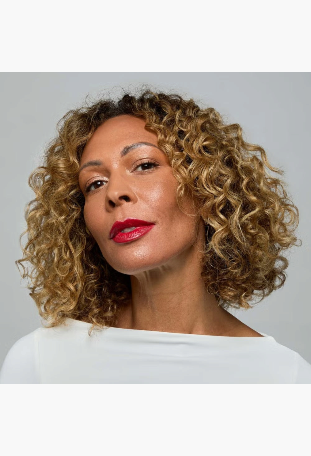GLAM MODA model with radiant skin and curly hair wearing a white top, showcasing a smooth and glowing makeup look.