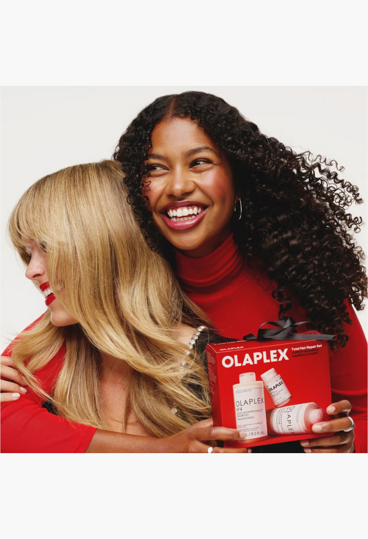Two smiling women holding the GLAM MODA Olaplex Total Hair Repair Set featuring bond-building shampoo and conditioner.